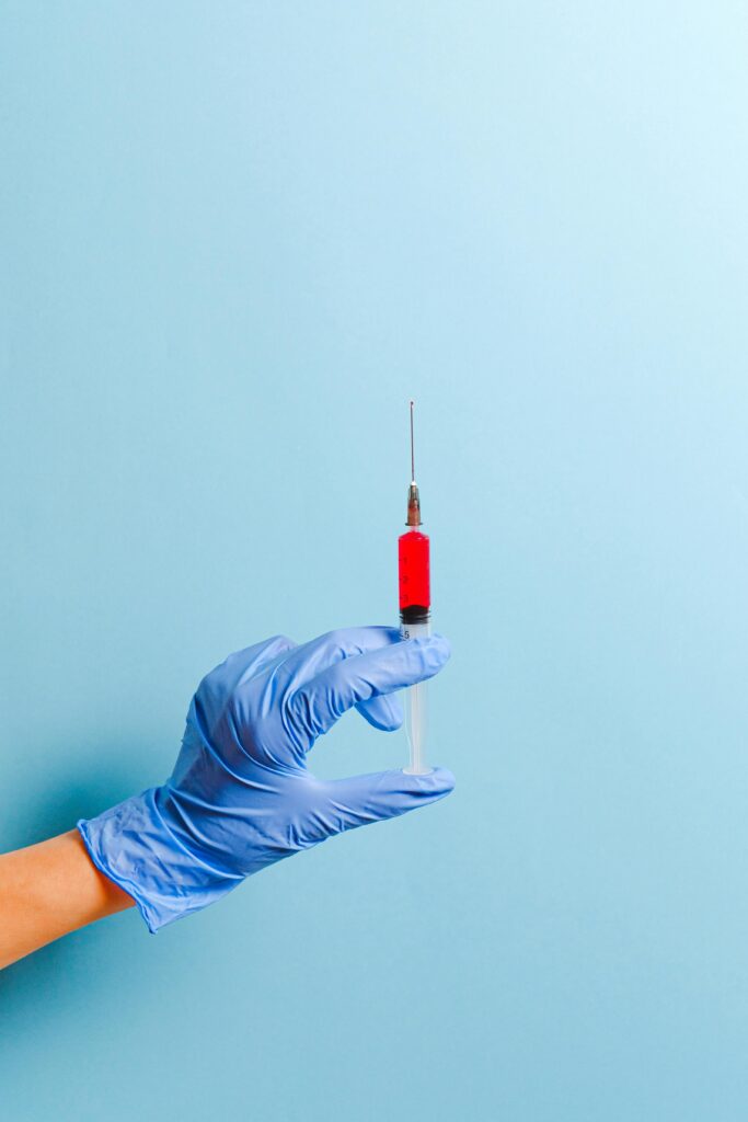 pexels photo 3786215 3786215 A gloved hand holds a syringe with red liquid, set against a blue background.